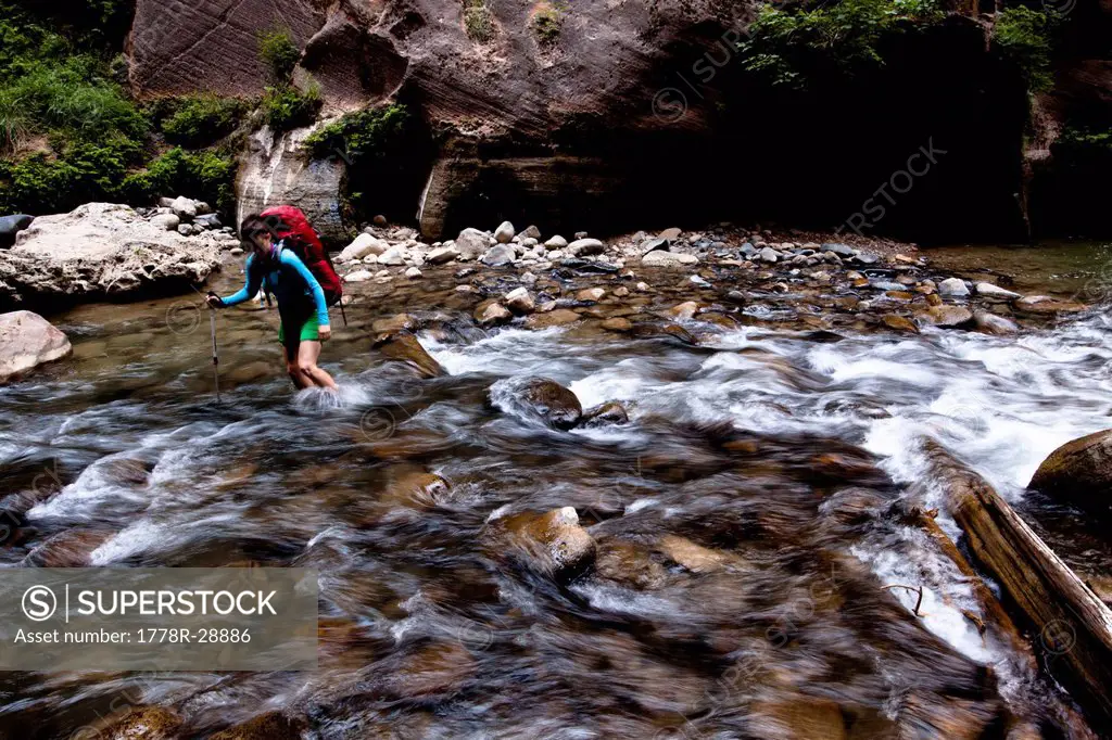 A woman uses a trekking pole to cross a section of the Virgin River during a backpacking trip through the Narrows in Zion National Park, in Springdale...