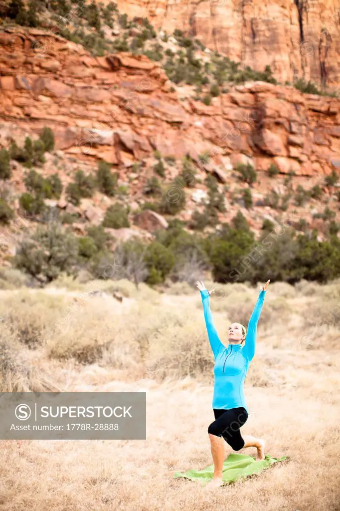 A young woman transitions into warrior one during a yoga session beneath The Watchman formation located at Zion National Park in Springdale, Utah.
