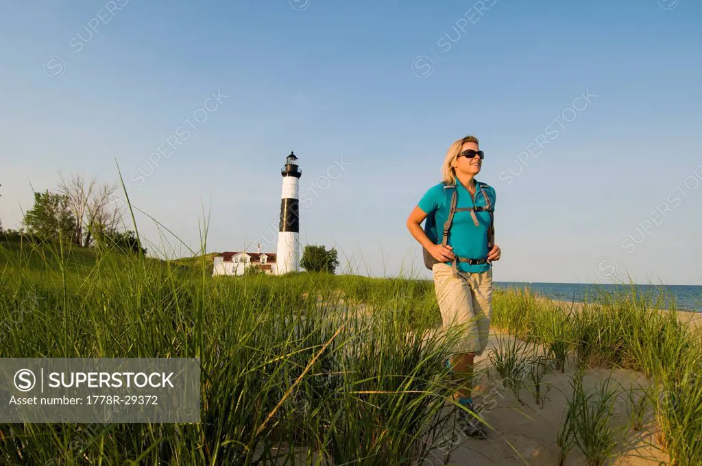 A woman hiking past Big Sable Point Lighthouse, Ludington State Park, Michigan.