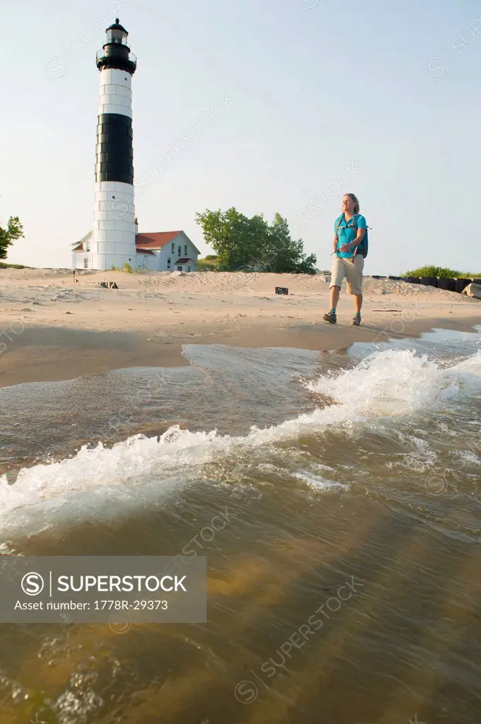 A woman hiking past Big Sable Point Lighthouse, Ludington State Park, Michigan.
