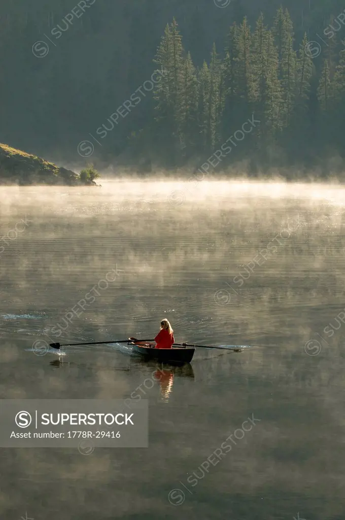 A woman rowing a scull boat a foggy morning near Creede, Colorado.