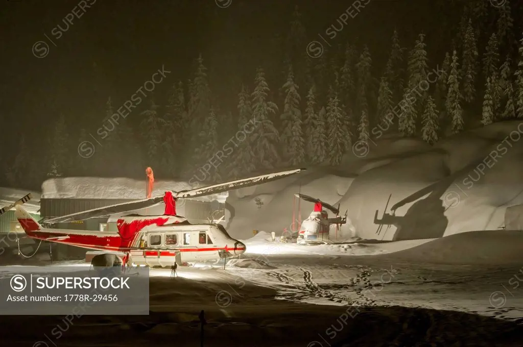 Helicopters used for heli-skiing parked in heavy snowfall at night.