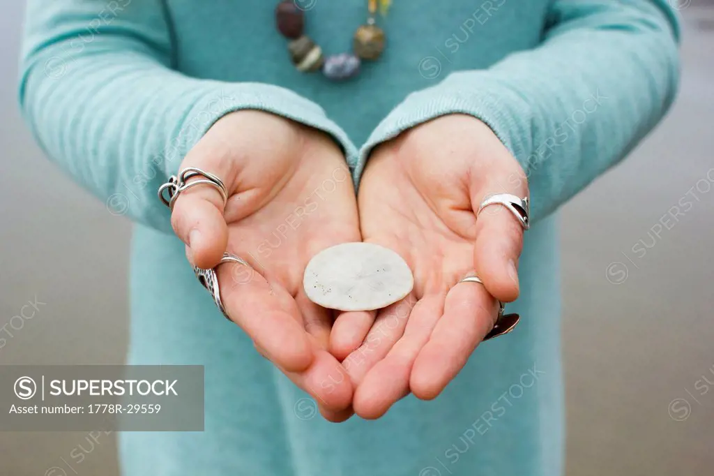 Image of young woman holding a sand dollar on the beach in Manzanita, Oregon.