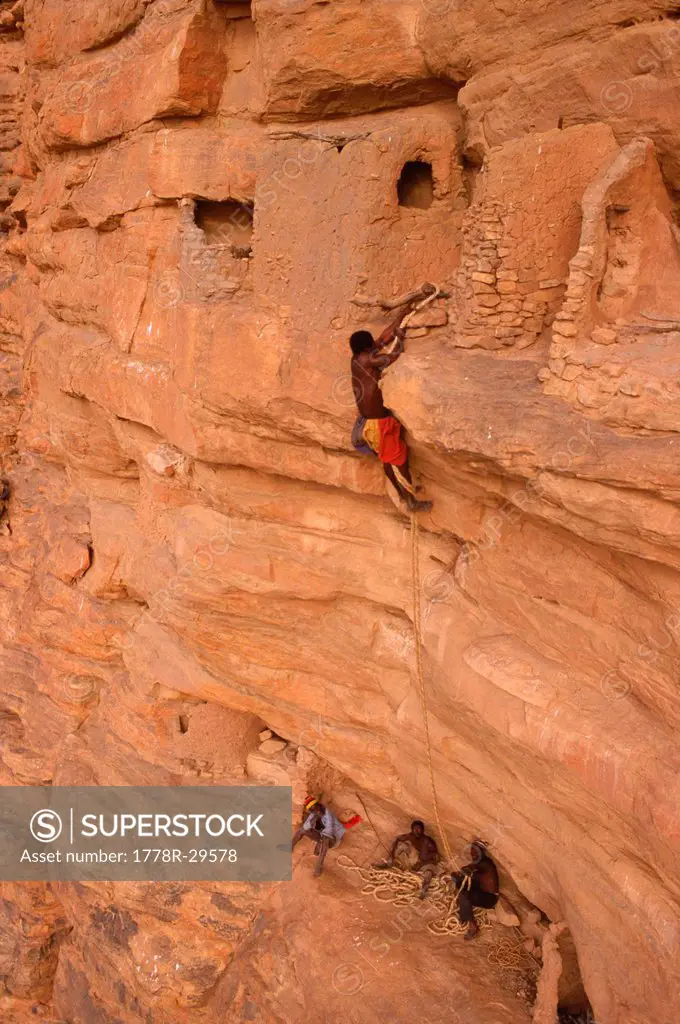 Tribal man climbing a rock cliff, Mali Dogon, Village of Pegua, Africa.