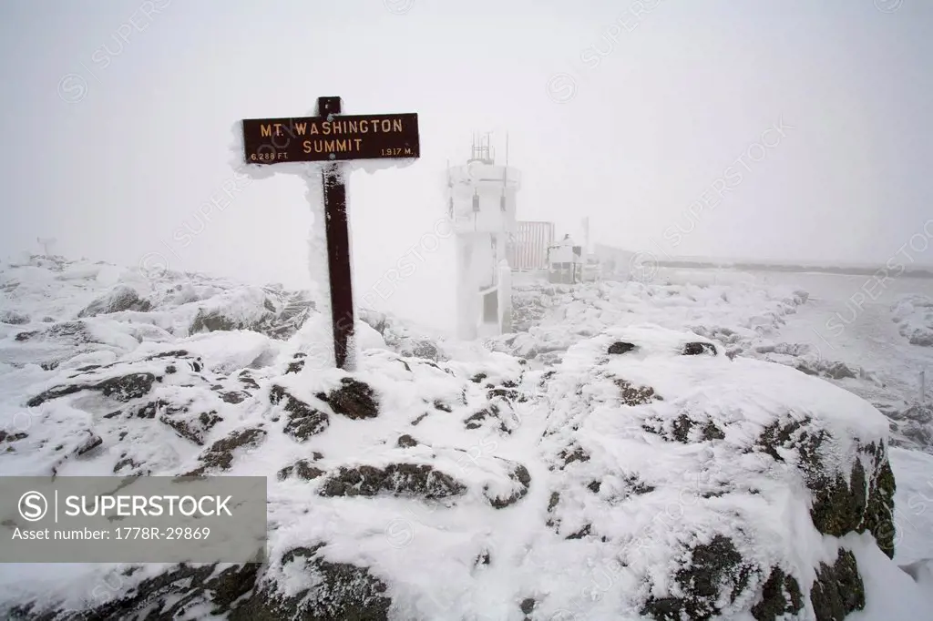 A snow and ice covered sign marks the summit of Mount Washington in the White Mountains of New Hampshire.