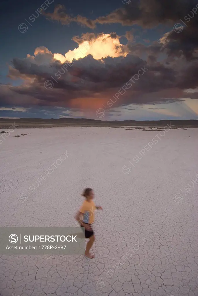 Woman runs on dry lake bed in desert.