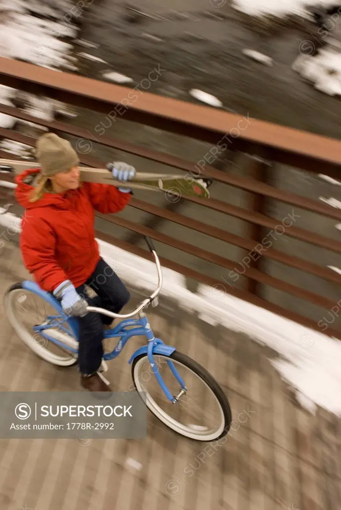 Woman bikes over bridge with skis.