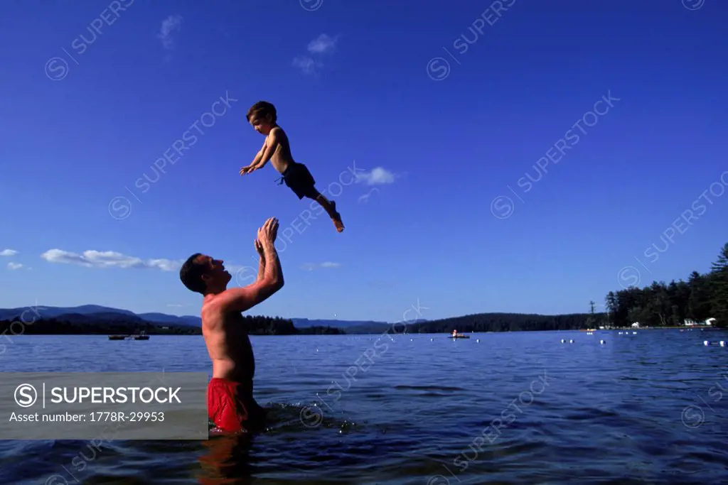 A father tosses his son into the air above Kezar Lake, Maine, USA.