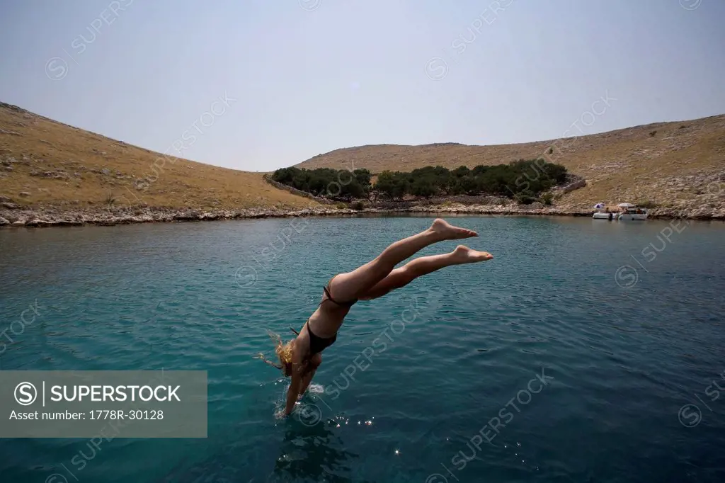 A young girl dives off of a boat into the waters of the blue Adriatic Sea.