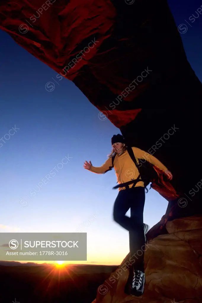 Woman hikes under arch at sunset.