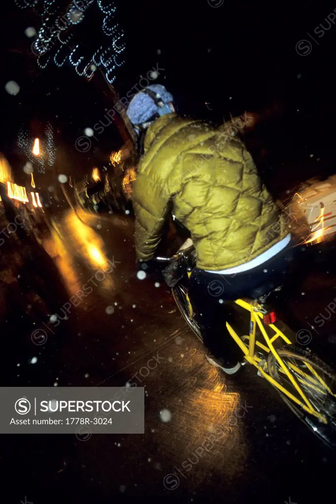 Woman bikes in snowstorm at night.