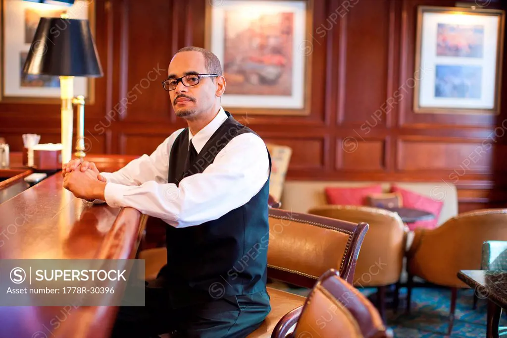 a waiter sits on a barstool at the edge of a bar