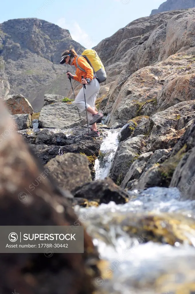 Backpacker jumps a stream while hiking in Chugach State Park near Anchorage, Alaska.