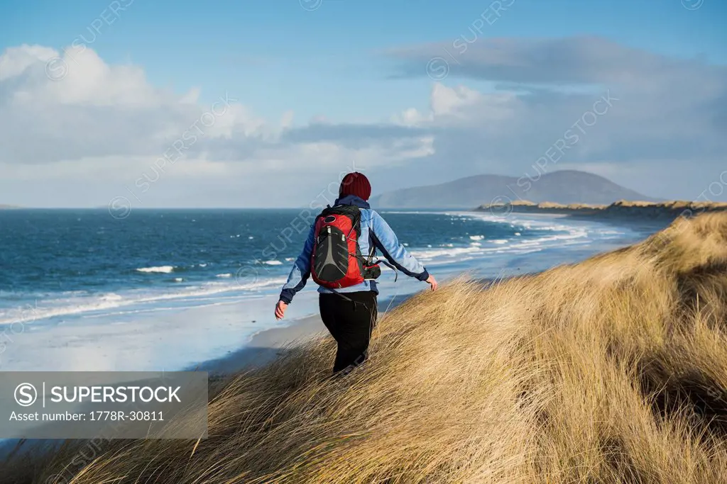Woman walks through coastal dune grass at west beach, Berneray, Outer Hebrides, Scotland