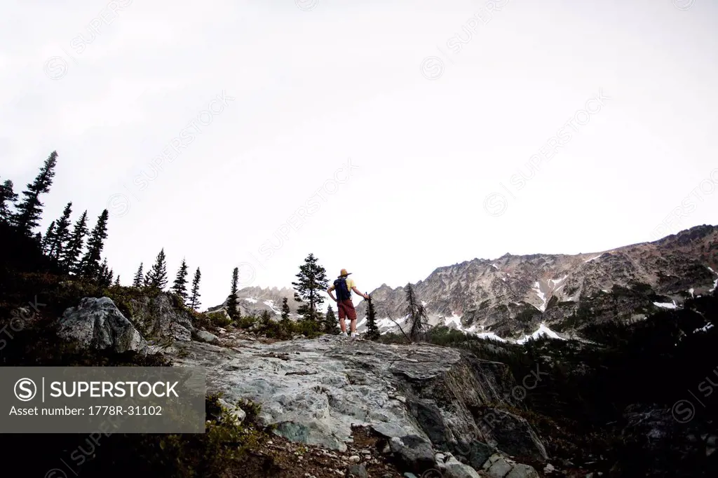 A male hiker on a trail as he attempts to summit a peak on a cloudy day in the North Cascades, WA.