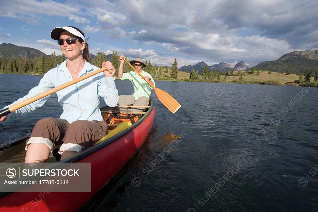 Woman and man in red canoe on lake.