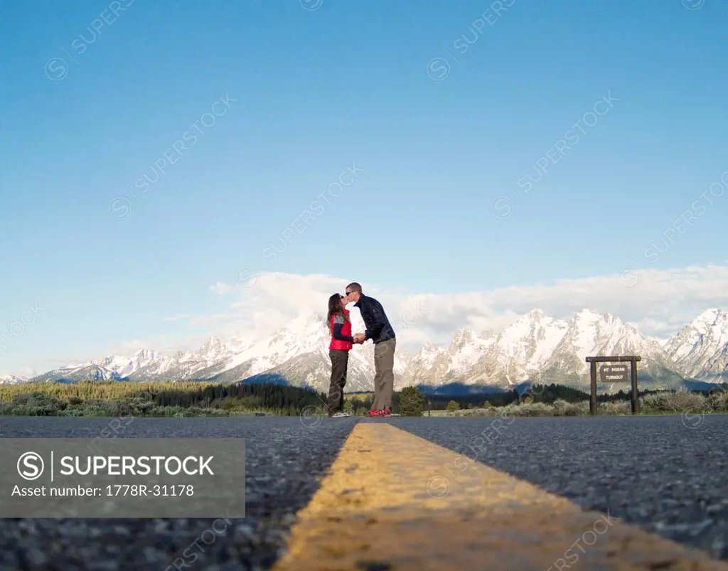 A young couple kisses with mountains in the background