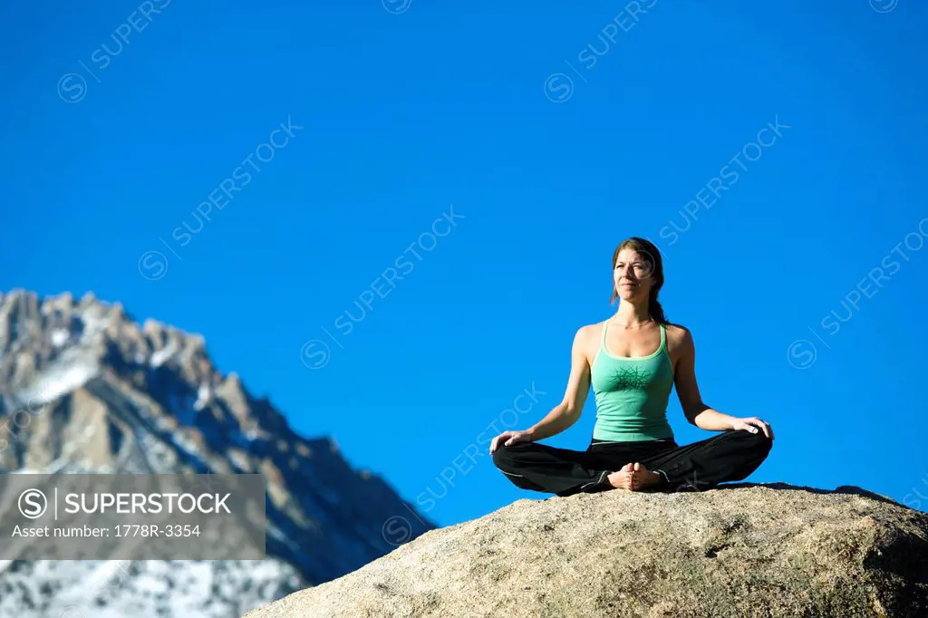 Woman doing yoga on boulder.