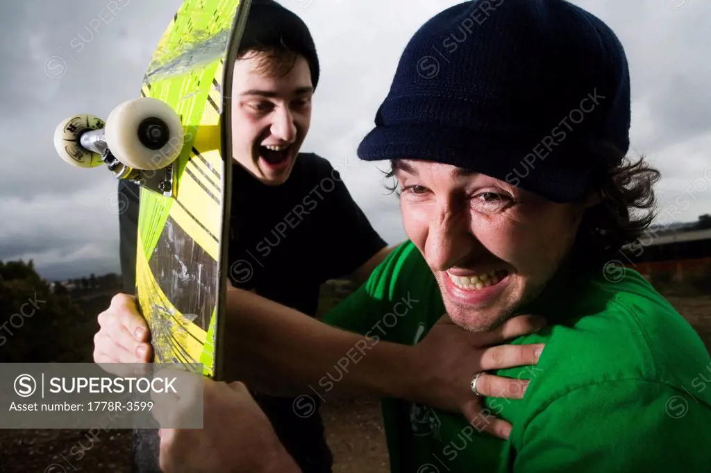 A skateboarder attacks the camera while the other holds him back.