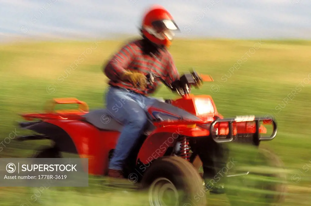 ATV driver riding fast through field.