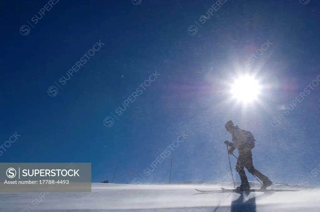 A man cross_country skiing against a bright blue sky in sunlight.