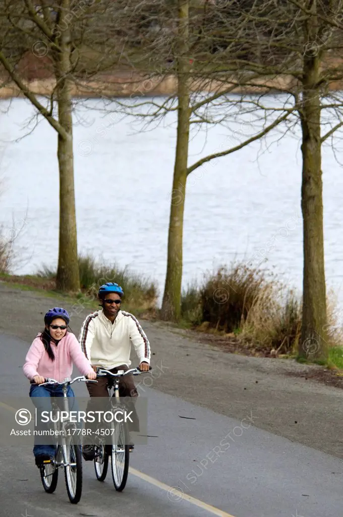A young couple ride bikes on a bike path near the ocean.
