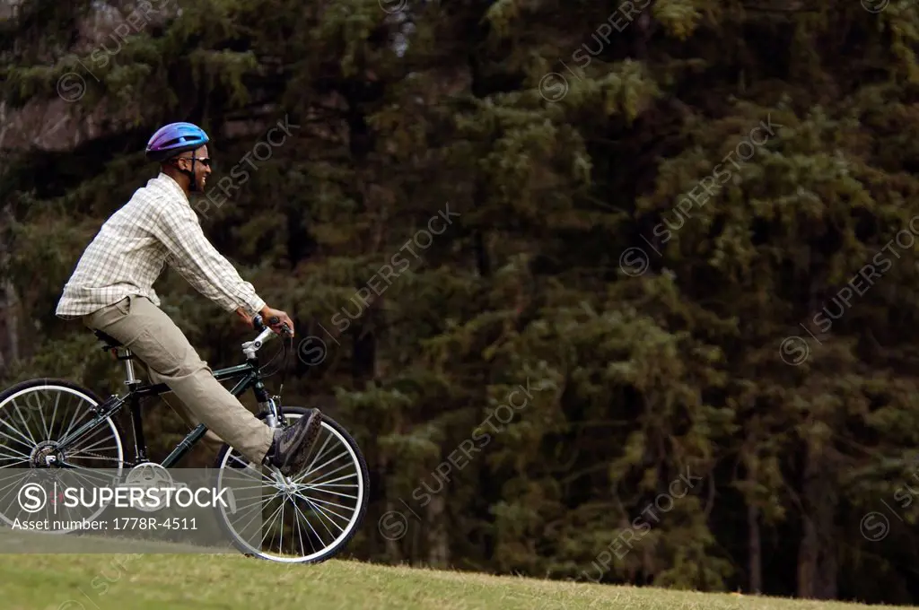 A carefree young African_American man rides a bike through a grassy field.