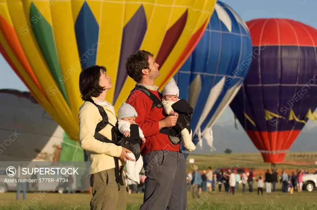 A family with twin babies watches hot air balloons launch during a festival.