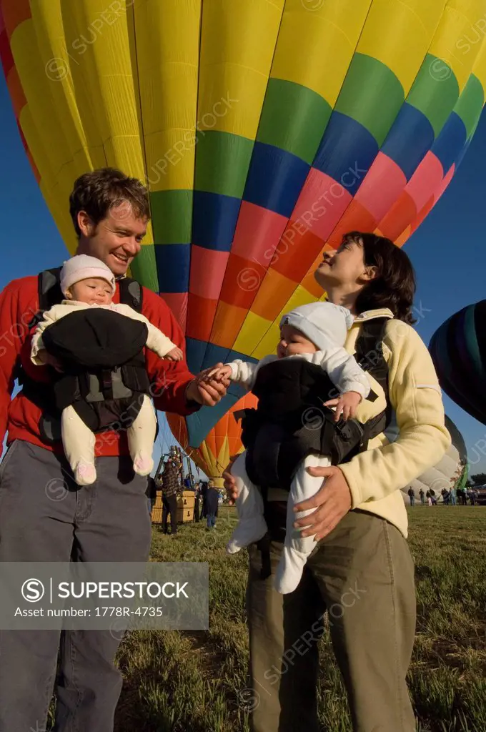 A family with twin babies watches hot air balloons launch during a festival.