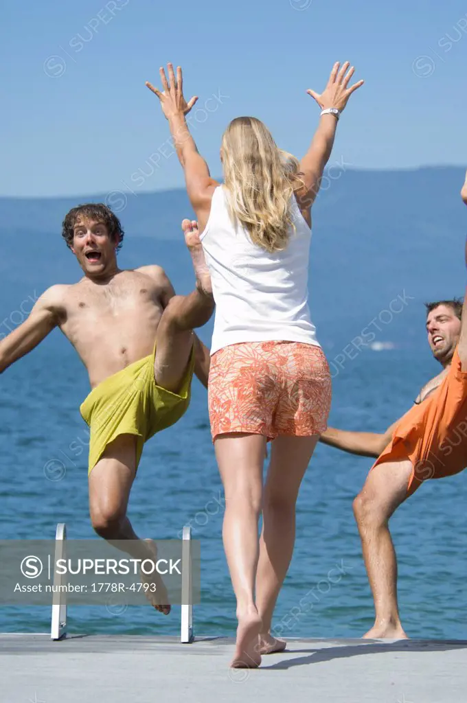 A young woman pushes her male friends into a lake.