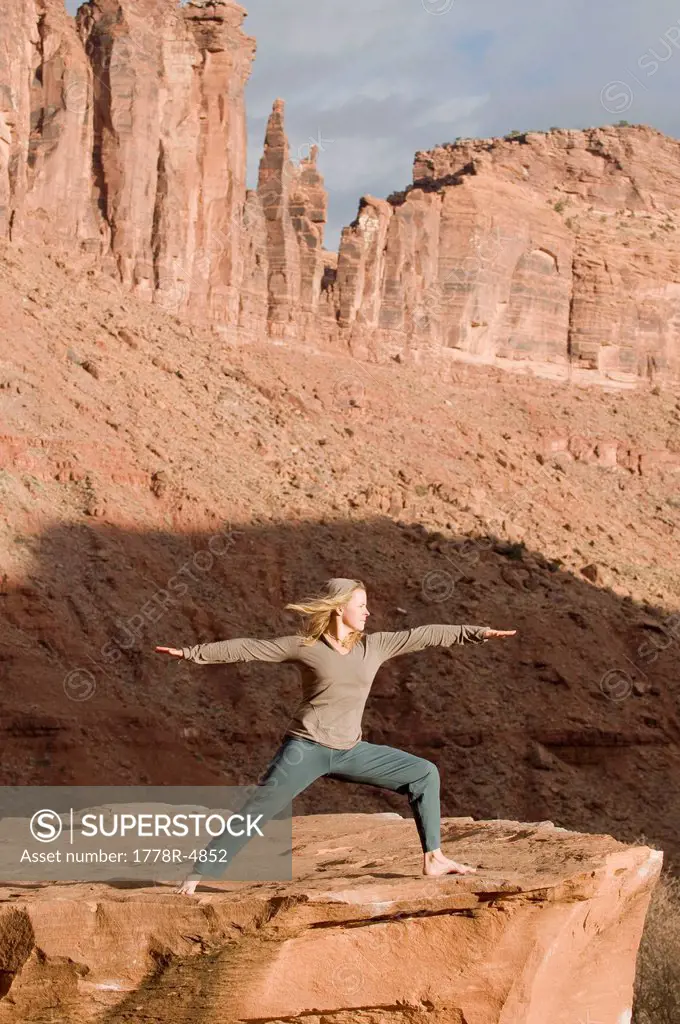 Woman in yoga pose on sandstone rock below sandstone towers, Moab, Utah.