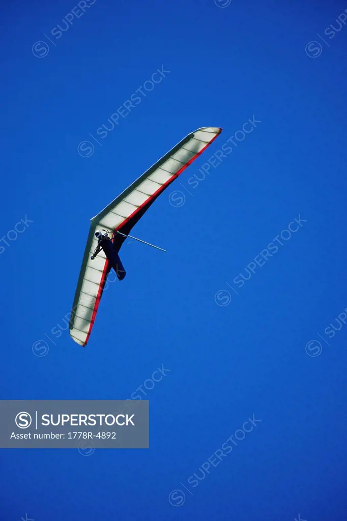 Hang glider soars the thermals against a blue sky.