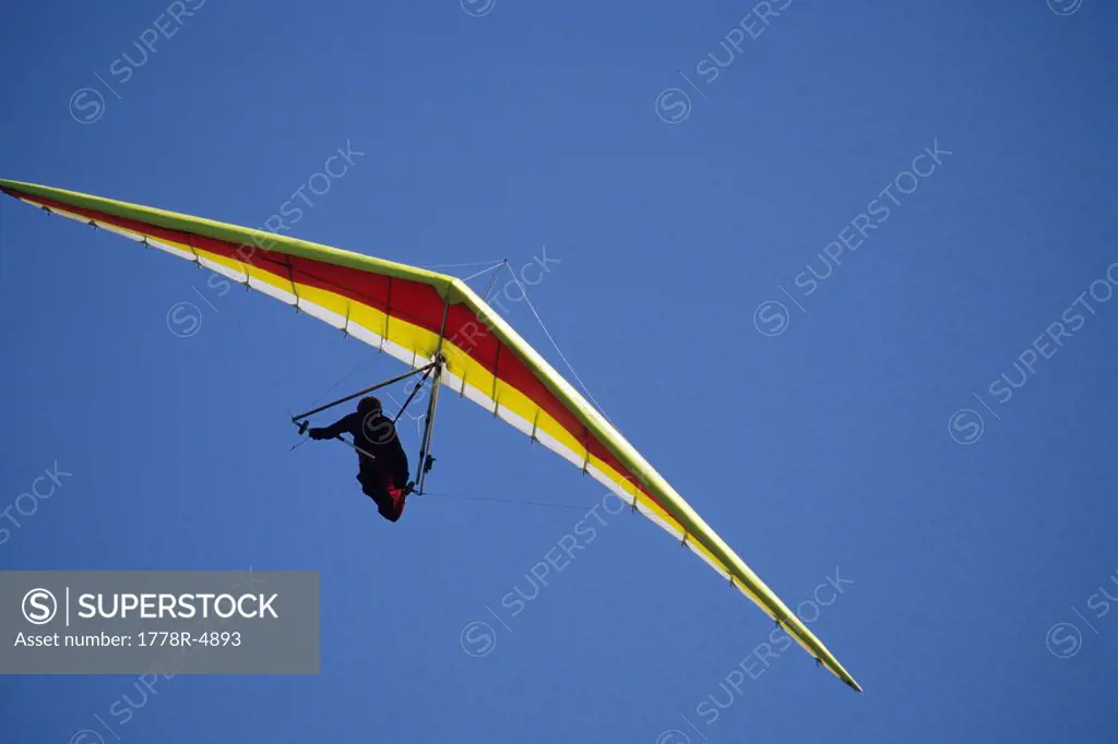 Hang glider banks into a turn against a blue sky.