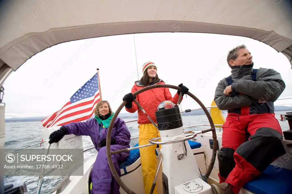 Three people in bright colored sailing gear out at sea.