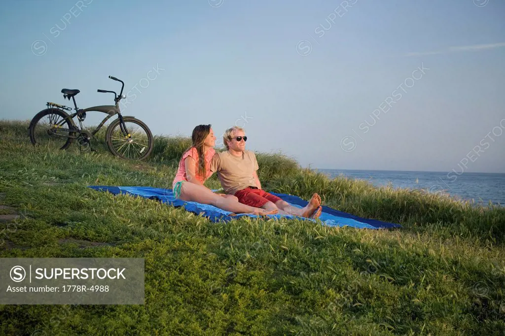 A couple sits on a blanket near the beach.