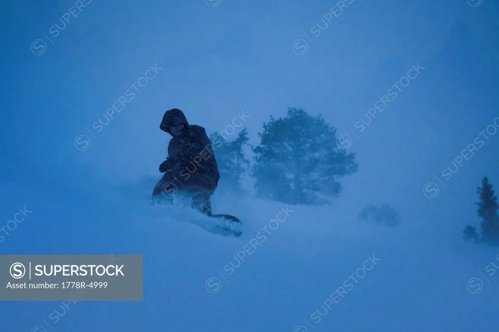 Snowboarder carving through powder snow in a dark storm.