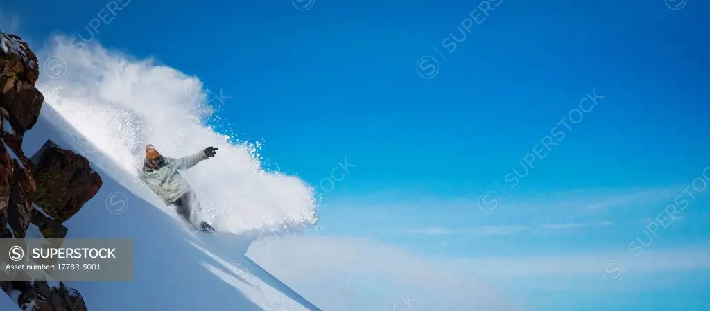 Snowboarder carving through powder snow in front of a blue sky.