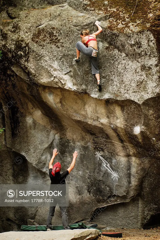 A woman bouldering with a spotter in Yosemite Valley, California, USA.