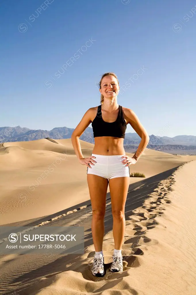A young woman in running clothes standing on a 200ft sand dune on a sunny day.