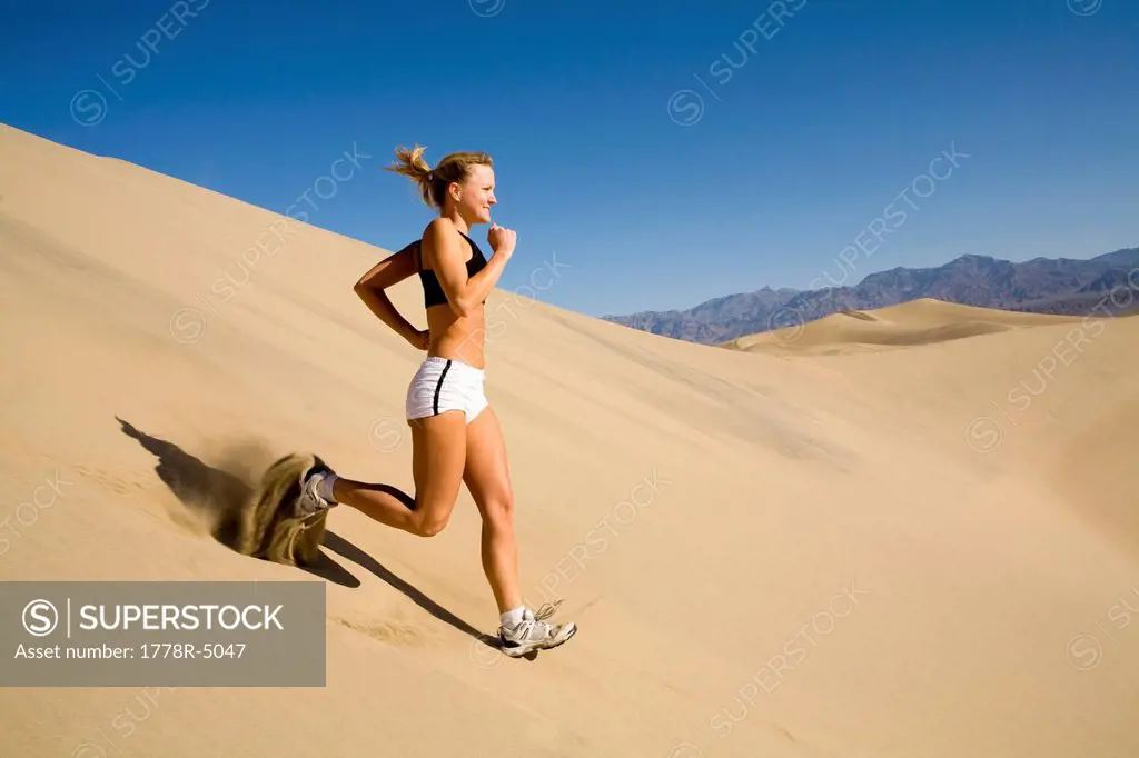 A young woman running down a steep sand dune in Death Valley, California.