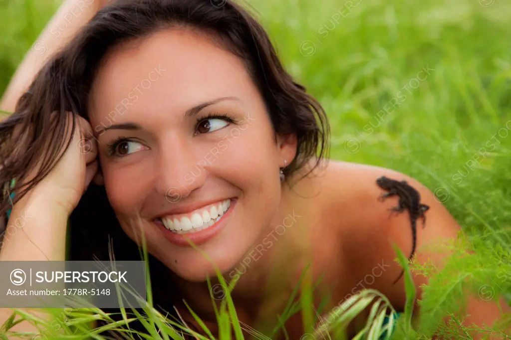 Happy young woman in a field of fresh grass smiles as a small lizard crawls up her shoulder.