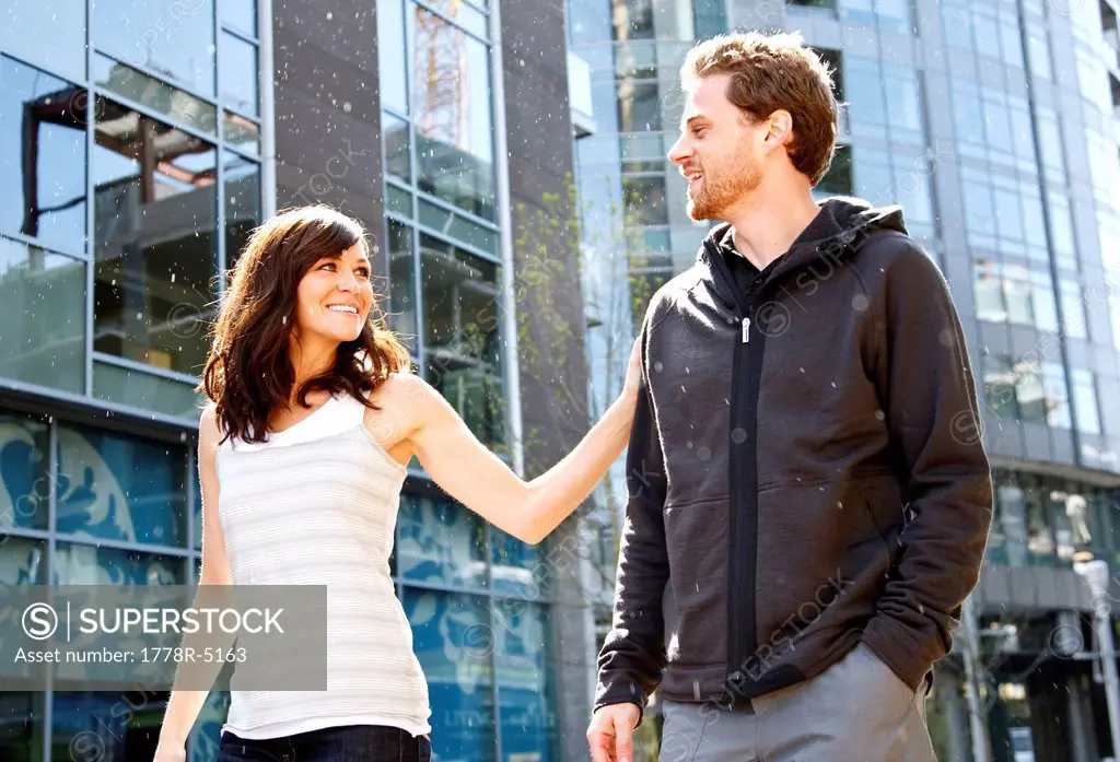 A man and woman walking in an urban part of the city as the sun highlights a light rain.