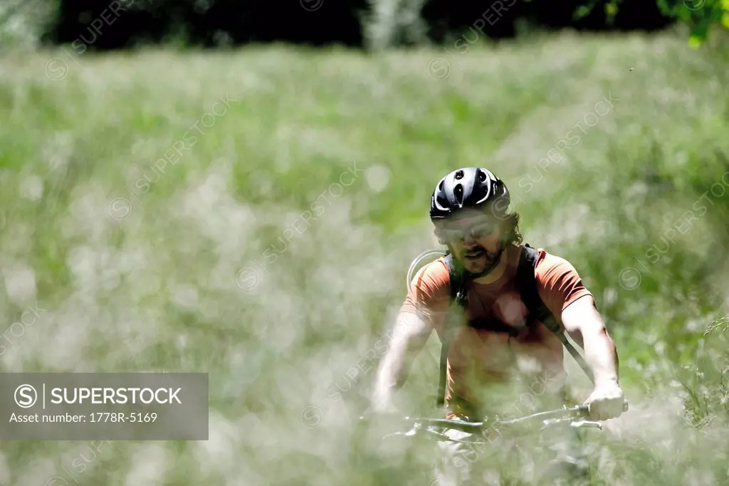 A mountain biker riding a single track trail through a grassy field.
