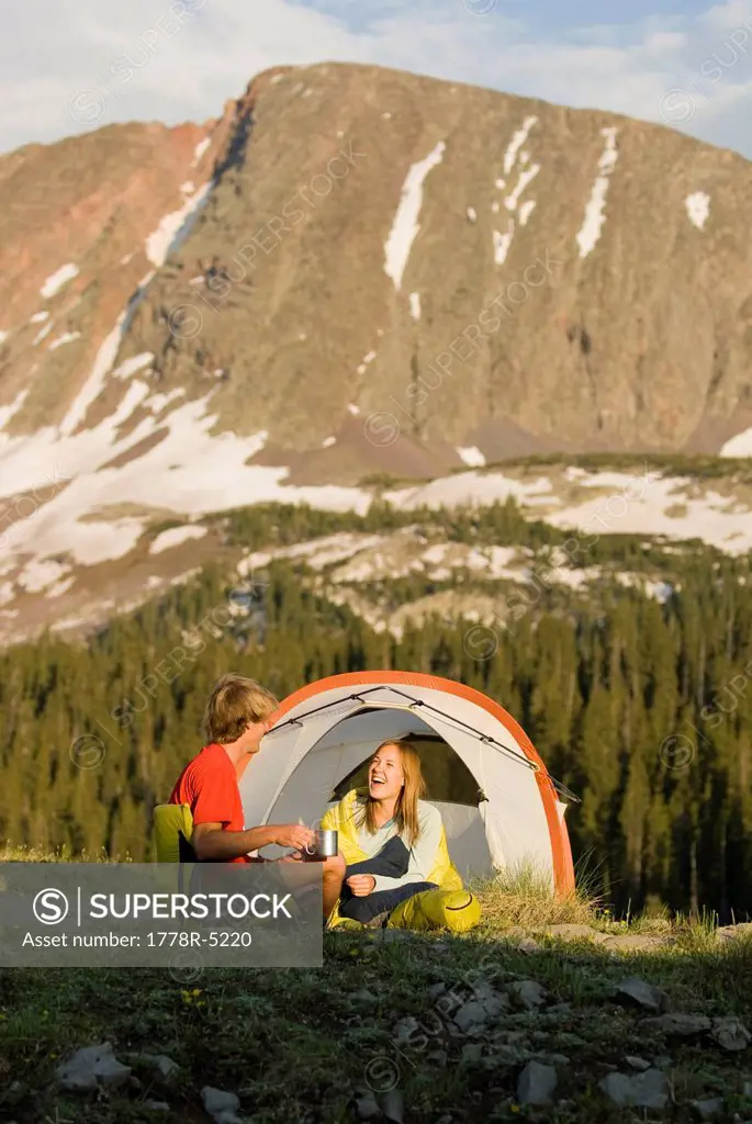 A young couple laughing in tent below a peak, San Juan National Forest, Colorado.