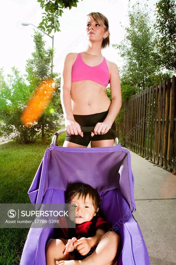An edgy_looking, athletic young woman with tattoos stops during a run on a suburban sidewalk with a baby in a jogging stroller.