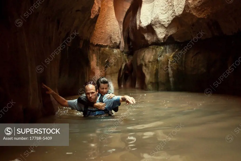 A couple wades through a cold pool in a slot canyon in Utah.