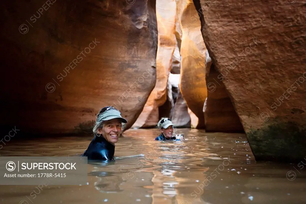 Two women wading through a deep pool in a slot canyon in Utah.
