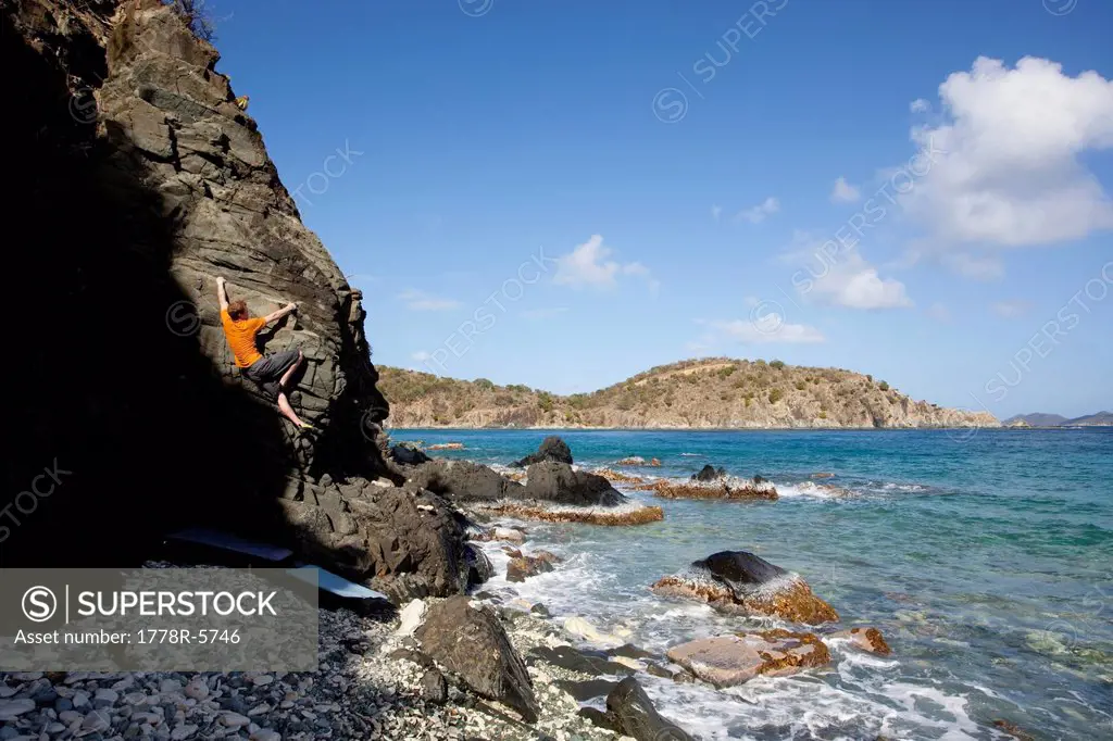 A man climbs out of the shadow on a beach boulder problem in the Caribbean.