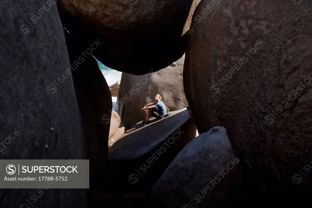 A man sits in the sunlight outside a cave of giant boulders which cover the southern tip of Virgin Gorda, The Baths National Park, British Virgin Isla...