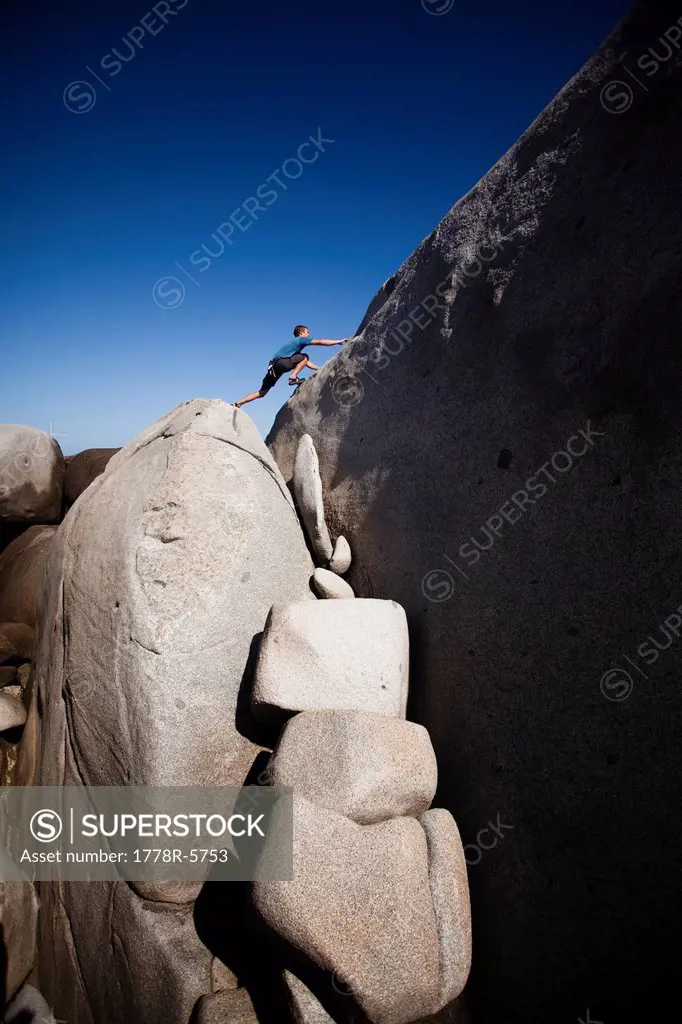 A man stretches out to explore atop giant boulders on the beach in The Baths National Park, Virgin Gorda.
